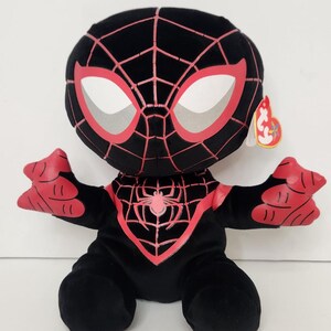 May include: A plush toy of the character Miles Morales, also known as Spider-Man. The toy is primarily black with red accents, including the spider-web design on the head and chest. The eyes are white with red outlines. The toy has a tag attached.