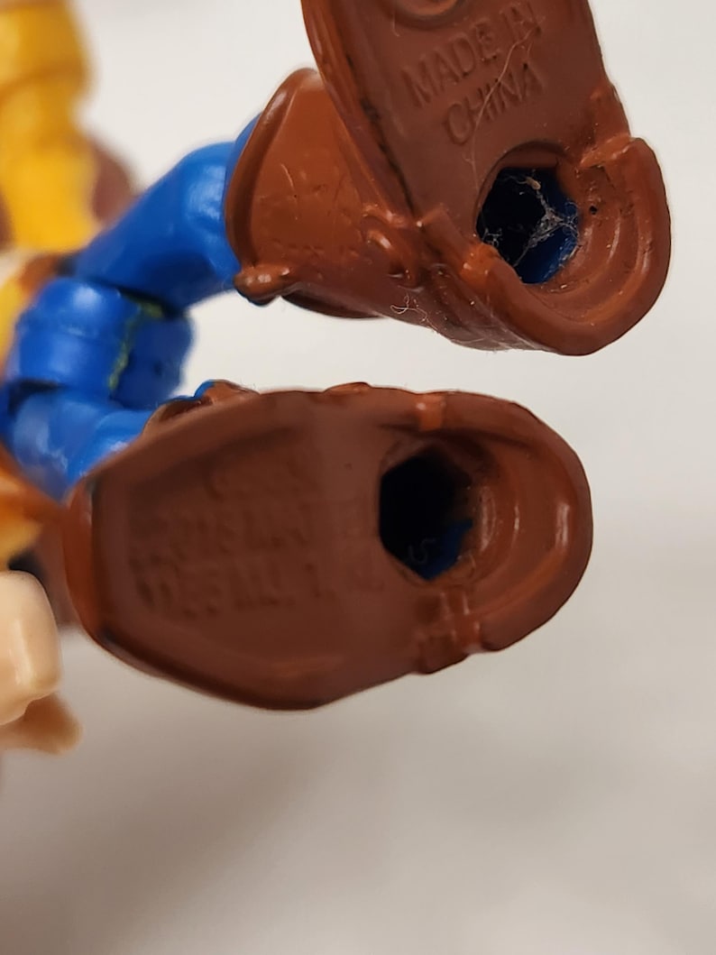 May include: Close-up of the feet of a plastic toy figure. The figure has brown boots, blue pants, and a yellow shirt. The words "MADE IN CHINA" are visible on the bottom of one boot.