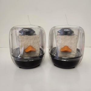 May include: Two penguin-shaped sushi molds. Each mold has a black base, a clear plastic cover, and a white rice block with an orange beak. A small knife is included in each mold.