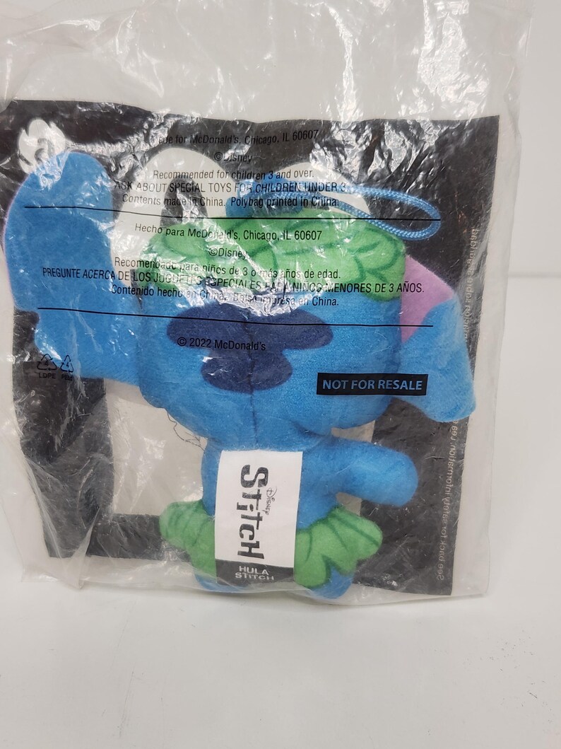 May include: A blue plush Stitch toy from the Disney movie, in a clear plastic bag. The toy has green accents and a tag that says "Stitch" and "Hula Stitch". The bag also has text that says "Not for Resale".