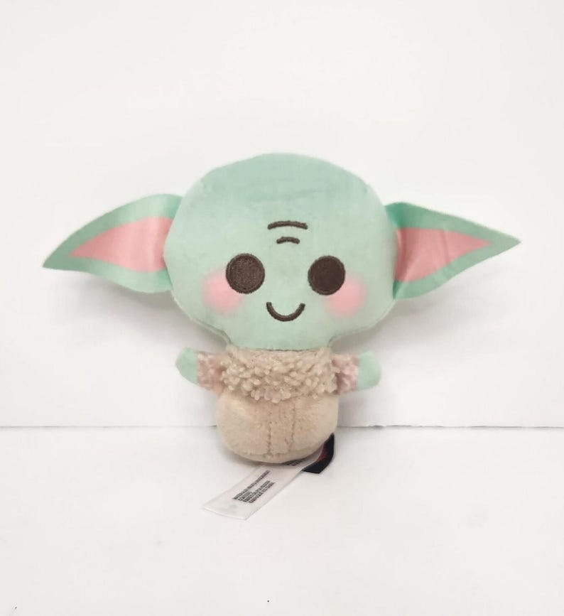 May include: A plush toy of a character with large ears, a green head, and a tan body. The toy has pink accents on the ears and cheeks, with a small tag attached. The character has a smiling expression.