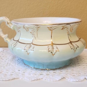 May include: A vintage white and blue ceramic chamber pot with gold leaf accents and a decorative handle.