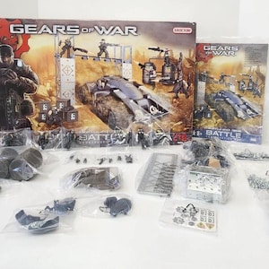 Puede incluir: Un juego de construcción de Gears of War con una caja que presenta una escena de batalla futurista. El juego incluye varias piezas de plástico, figuras y un vehículo tipo tanque. La caja y los componentes se muestran sobre una superficie blanca.