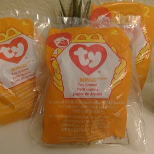 May include: Three sealed orange plastic packages of Ty Bongo toy animals. Each package features the Ty heart logo and the McDonald's logo. Text on the packages reads "Bongo Toy Animal" in English, French, and Spanish.