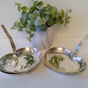 May include: Two silver heart-shaped dishes with handles. The dishes are empty and have a shiny finish.