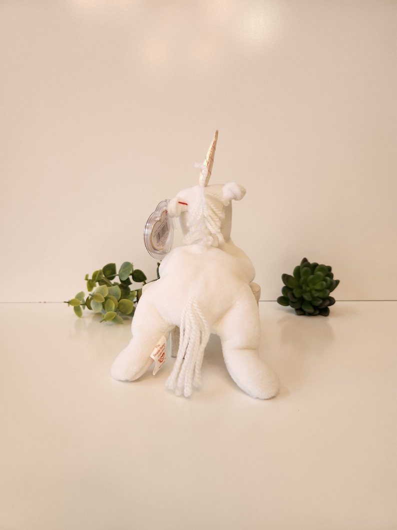 K&ouml;nnte beinhalten: Wei&szlig;es Pl&uuml;sch-Einhorn-Spielzeug mit goldenem Horn und wei&szlig;em Schwanz. Das Spielzeug sitzt auf einer wei&szlig;en Oberfl&auml;che.