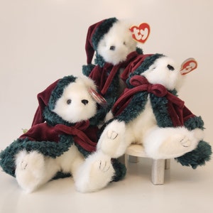 May include: Three white plush teddy bears wearing green and burgundy velvet coats with red and white beanie hats. The bears are sitting on a white stool.
