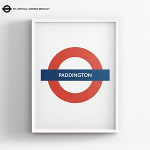 May include: A framed wall print featuring the iconic London Underground roundel logo with a red circle and a horizontal blue bar containing the white text PADDINGTON. The top left corner includes the text TFL OFFICIAL LICENSED PRODUCT.