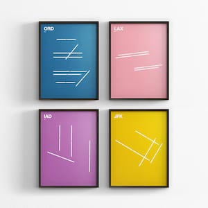May include: Four framed art prints with colorful backgrounds: blue (ORD), pink (LAX), purple (IAD), and yellow (JFK). Each print features white geometric line designs. The frames are black, and the prints are displayed on a white wall.
