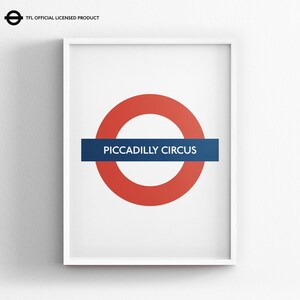 May include: A framed wall print featuring the iconic London Underground roundel logo with a red circle and a horizontal blue bar containing the white text PICCADILLY CIRCUS. The top left corner includes the text TFL OFFICIAL LICENSED PRODUCT.