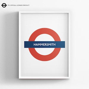 May include: A framed wall art print featuring the iconic London Underground roundel logo in red and blue with the text HAMMERSMITH in white capital letters. The design includes a small TFL OFFICIAL LICENSED PRODUCT logo in the top left corner.