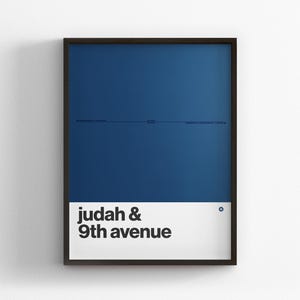 May include: A framed rectangular wall art print featuring a deep blue background with a thin horizontal line and small text in the center. The bottom section is a white horizontal band with the black text "judah & 9th avenue" and a small blue circle icon.