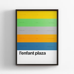 May include: Framed art print with horizontal bands of yellow, green, gray, orange, and blue. The text "l'enfant plaza" is in white on a white background at the bottom of the print. The frame is black.
