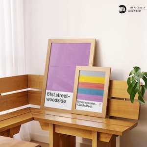 May include: Two framed posters with wooden frames. One poster has a purple background with white text that reads "61st street-woodside". The other poster has a colorful striped design with text that reads "times square-42nd street".