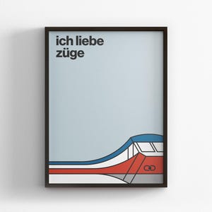 Puede incluir: Impresión artística enmarcada con el texto alemán "ich liebe züge", que significa "Amo los trenes". La obra presenta un diseño de tren estilizado en rojo, blanco y azul sobre un fondo azul claro. La impresión está en un marco negro.