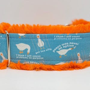 May include: A blue dog collar with a pattern of white geese and text. The collar has orange faux fur trim. The text includes phrases like "Peace was never an option" and "I think I will cause problems on purpose."
