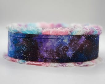 May include: A dog collar with a galaxy print in shades of blue, purple, and black. The collar is trimmed with fluffy faux fur in pastel pink, blue, and white. The collar is a pet accessory.