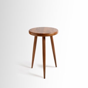 May include: A round wooden stool with three legs. The stool is made of dark brown wood and has a smooth, polished finish.