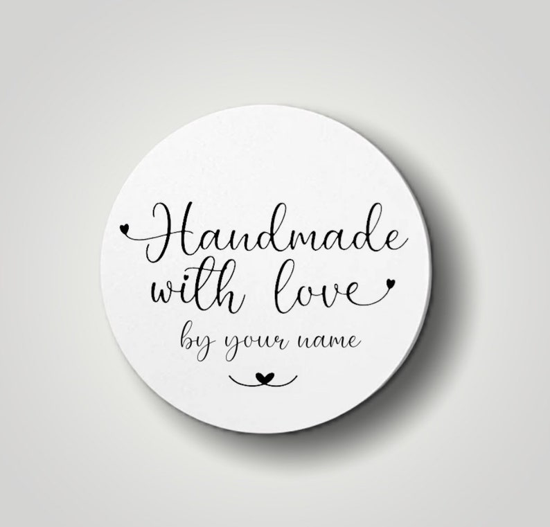 Może przedstawiać: Biała okrągła naklejka z czarnym tekstem, kt&oacute;ry brzmi "Handmade with love by your name" z małym symbolem serca nad tekstem i małym symbolem serca pod tekstem.
