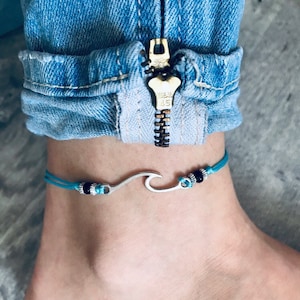 May include: A turquoise blue ankle bracelet with a silver wave charm and black beads.