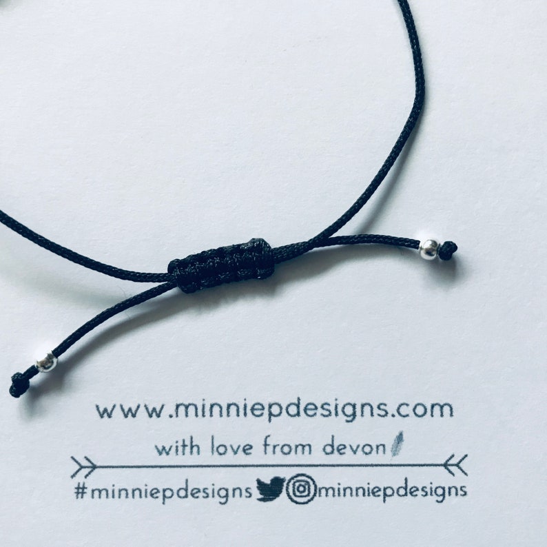 May include: Black adjustable bracelet with silver beads and a knot closure. The bracelet has a tag attached with the text "www.minniepdesigns.com with love from devon #minniepdesigns @minniepdesigns"