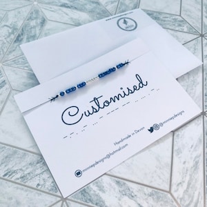 May include: A white card with the word "Customised" written in black cursive. The card also includes the text "Handmade in Devon" and an email address and Twitter handle for the business.