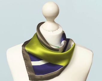 May include: A square silk scarf with a geometric design, displayed on a white mannequin. The scarf features a vibrant color palette of lime green, navy blue, white, and gray. The scarf is approximately 24 inches by 24 inches.