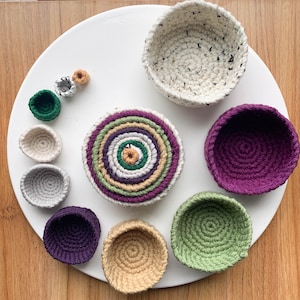 May include: A collection of 10 crocheted baskets in various colors and sizes. The baskets are made of yarn and have a variety of patterns. The baskets are arranged on a white surface.