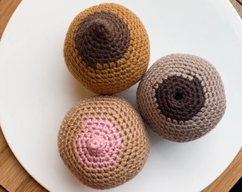 Op de afbeelding: Drie bolvormige, gehaakte objecten met verschillende kleurcombinaties. Eén is goudbruin met een donkerbruin midden, één is lichtbeige met een roze midden en één is taupe met een donkerbruin midden, allemaal met een textuur van garen.