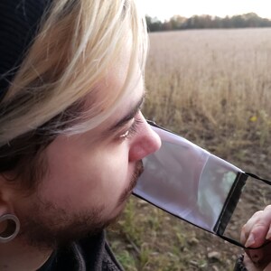 May include: A person wearing a black beanie and a white face mask with a black trim. The person is looking off to the side and has blonde hair.