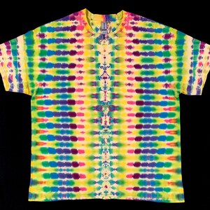 Op de afbeelding: Een tie-dye t-shirt met een levendig patroon van horizontale strepen in geel, groen, paars, blauw en roze. Het shirt heeft een ronde hals en korte mouwen. Het tie-dye ontwerp is symmetrisch in het midden.