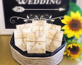 May include: A black tray with a burlap trim holds small white soap bars wrapped in twine and decorated with dried flowers. The tray is surrounded by sunflowers.