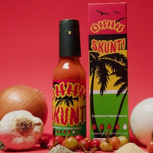 May include: A red, yellow, and green bottle of "Ohhh Skunti!" Caribbean pepper sauce with a palm tree design. The bottle is surrounded by onions, garlic, spices, and red peppers.