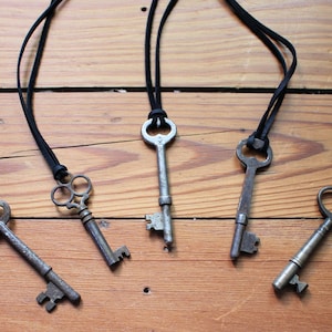 May include: Five antique keys on black leather cords. The keys are different shapes and sizes, and some have intricate details.