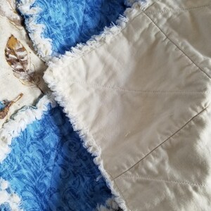 K&ouml;nnte beinhalten: Nahaufnahme einer handgefertigten Steppdecke mit einem blauen und wei&szlig;en gemusterten Stoff und einem wei&szlig;en Stoff mit ausgefransten Kanten.