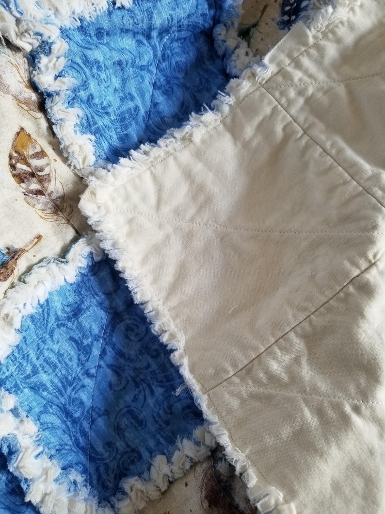 K&ouml;nnte beinhalten: Nahaufnahme einer handgefertigten Steppdecke mit einem blauen und wei&szlig;en gemusterten Stoff und einem wei&szlig;en Stoff mit ausgefransten Kanten.
