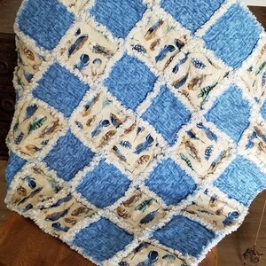K&ouml;nnte beinhalten: Eine blaue und cremefarbene Patchwork-Decke mit Federndruck. Die Decke ist aus weichem, flauschigem Stoff gefertigt und hat einen ausgefransten Rand.