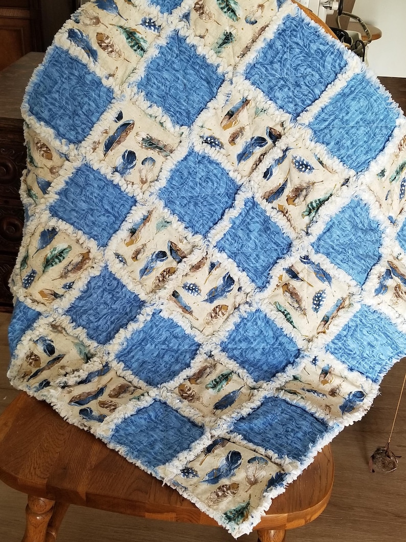 K&ouml;nnte beinhalten: Eine blaue und cremefarbene Patchwork-Decke mit Federndruck. Die Decke ist aus weichem, flauschigem Stoff gefertigt und hat einen ausgefransten Rand.