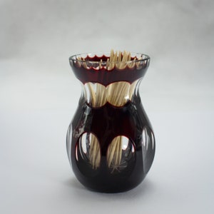 Op de afbeelding: Een doorzichtige glazen tandenstokerhouder met een rode rand en een uitgesneden ontwerp. De houder is gevuld met houten tandenstokers.