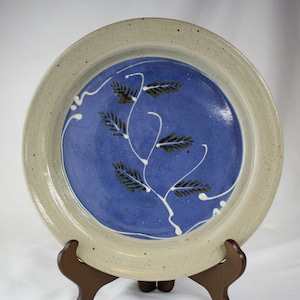 May include: A ceramic plate with a blue glaze and a white rim. The plate has a design of white and gold stylized leaves on a blue background.