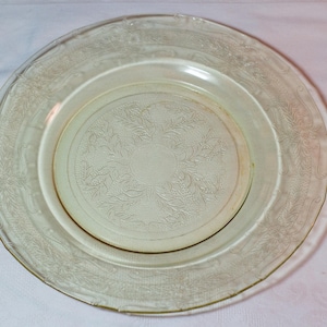 Puede incluir: Un plato de vidrio transparente con un delicado patrón floral alrededor del borde. El plato tiene un tono ligeramente amarillento.