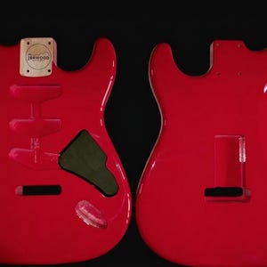 Könnte beinhalten: Zwei rote Gitarrenkorpusse, einer zeigt die Vorderseite mit Aussparungen für Tonabnehmer und Bedienelemente, der andere die Rückseite. Der vordere Korpus hat eine kleine Holzplatte mit dem Text "JRRWOOD". Die Korpusse sind glänzend und scheinen neu zu sein.