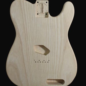 Könnte beinhalten: Unfertiger Gitarrenkorpus aus hellem Holz mit Aussparungen für Tonabnehmer, Bedienelemente und Hals. Der Korpus hat eine natürliche Holzmaserung und einen Stempel mit der Aufschrift "JBRWOOD". Der Gitarrenkorpus ist für eine E-Gitarre mit massivem Korpus konzipiert.