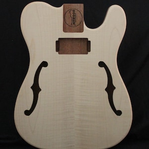 Peut inclure: Corps de guitare électrique inachevé en bois clair. Il présente deux ouïes en forme de f, une cavité rectangulaire pour les micros et une poche de manche avec un petit logo rond indiquant "JERWOOD". Le corps présente un grain de bois lisse et naturel.