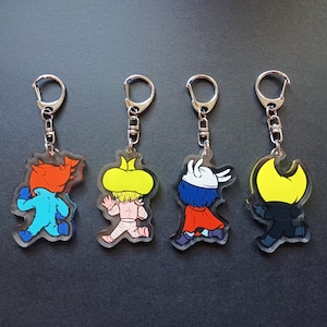 Puede incluir: Cuatro llaveros coloridos con personajes de dibujos animados. Cada llavero est&aacute; hecho de acr&iacute;lico transparente y presenta un personaje diferente con un esquema de color amarillo, azul, rojo y negro.