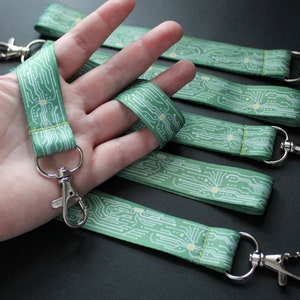 Pode incluir: Um conjunto de cinco chaveiros com padrão verde e branco com um design de placa de circuito. Cada chaveiro tem um anel de metal prateado.