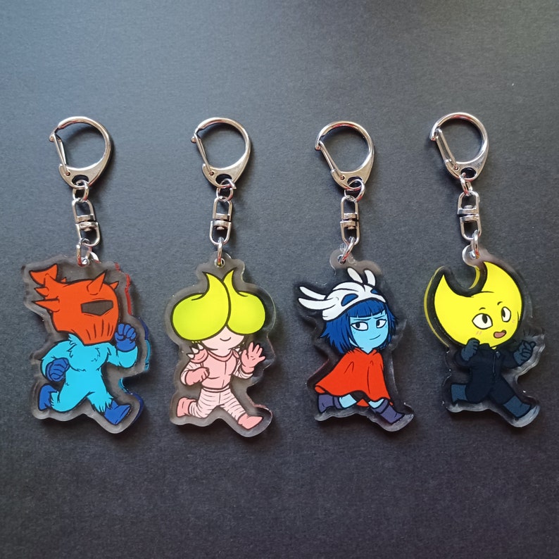 Puede incluir: Cuatro llaveros coloridos con personajes de dibujos animados. Cada llavero tiene un anillo de metal plateado y un dije de acr&iacute;lico transparente. Los personajes son un caballero azul, una criatura amarilla, una criatura rosa y una criatura azul con una capa roja.