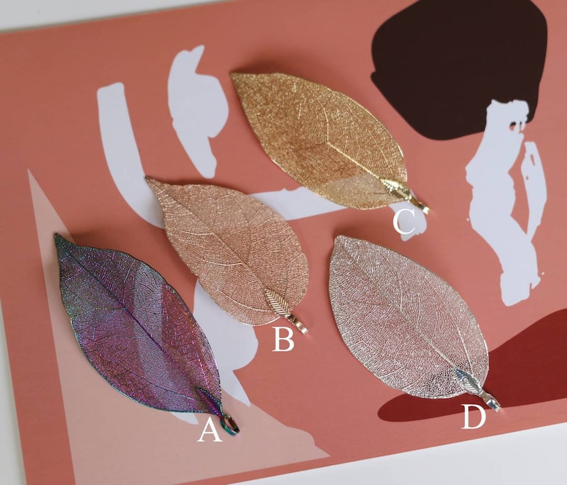 May include: Four delicate leaf-shaped pendants with a metallic finish. The pendants are in shades of gold, pink, silver, and iridescent purple. Each pendant has a small loop at the top for attaching to a chain or cord.