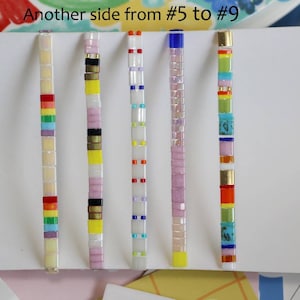 Pu&ograve; includere: Cinque braccialetti colorati con perline e diversi motivi. I braccialetti sono disposti orizzontalmente su uno sfondo bianco. Il testo "Another side from #5 to #9" &egrave; scritto nella parte superiore dell'immagine.