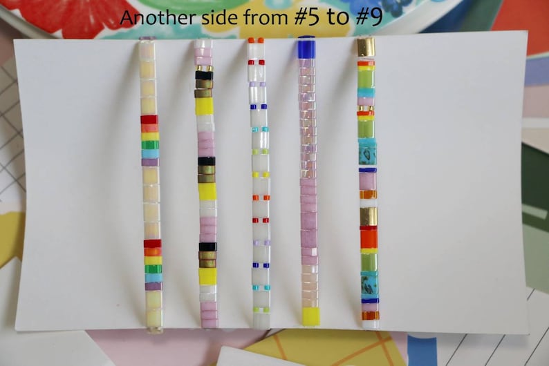 Pu&ograve; includere: Cinque braccialetti colorati con perline e diversi motivi. I braccialetti sono disposti orizzontalmente su uno sfondo bianco. Il testo "Another side from #5 to #9" &egrave; scritto nella parte superiore dell'immagine.